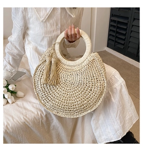 Detailed view of handmade woven straw handbag with ring handle and tassel in natural beige