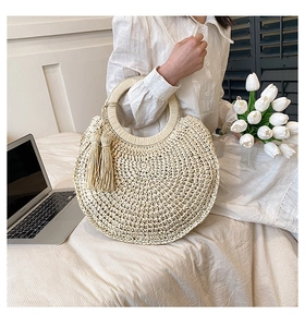 Detail of hand-woven straw handbag with round handle and decorative side fringe tassels
