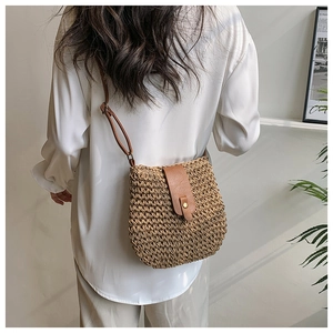 Detail of woven straw crossbody bag with brown leather strap and metal magnetic snap closure