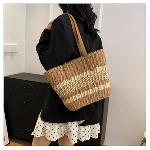 Lifestyle view of woven straw tote bag with striped pattern and brown leather straps