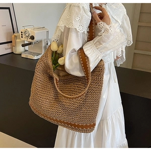 Detail of woven straw tote bag with brown leather trim worn by woman in lace dress
