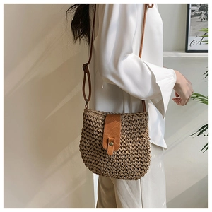 Close-up of handwoven straw crossbody bag with brown faux leather flap and brass buckle