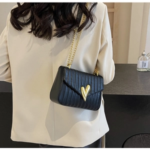 Detail of black quilted crossbody bag with golden heart clasp and metal chain strap
