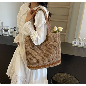 Brown woven straw tote bag held by a model in a cozy cafe setting, 2024 fashion style