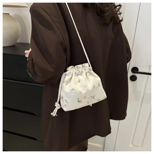 Detail of floral embroidered satin drawstring bucket bag showing texture and strap