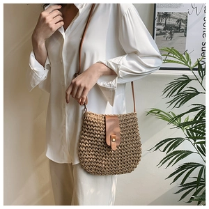 Close-up of woven straw crossbody bag with brown leather flap and adjustable strap details