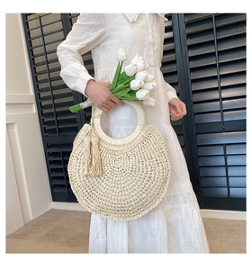 Detail of cream woven handbag with circular handle and elegant side tassel accents