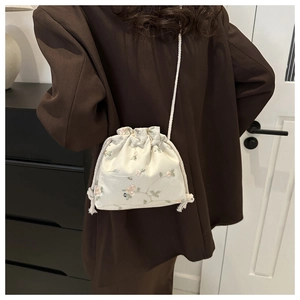 Detail view of a cream crossbody bag with floral embroidery worn over a dark brown blazer
