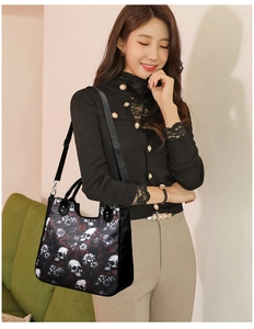 Detail of crossbody tote bag featuring gothic skull print and leather handles on model