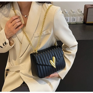 Detail of black quilted crossbody bag with golden heart-shaped clasp and metal chain strap
