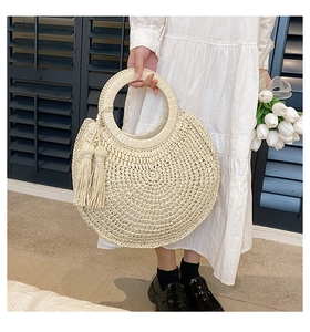 Detail of half-moon beige straw handbag with round handle and side tassel accents