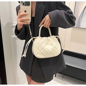 Detail of a creamy white quilted crossbody bag with drawstring closure and top handle