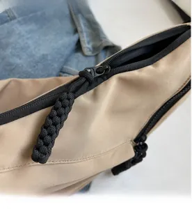 Detailed close-up of beige nylon crossbody bag with black cord zipper pulls and high texture