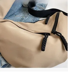 Detail of khaki nylon crossbody bag with black woven strap and braided zipper puller