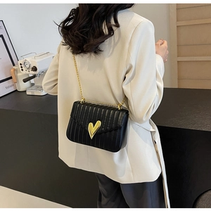 Detail of black quilted PU leather crossbody bag with a golden heart-shaped metal lock clasp