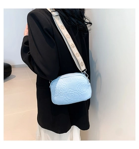 Détail d'un petit sac bleu clair avec gaufrage de camélia et large bandoulière imprimée