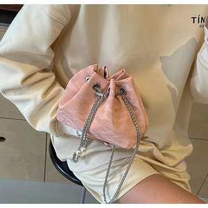 Detail of light pink bucket bag with pleated velvet texture and silver chain strap with pearls