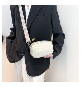 Detail of cream crossbody bag featuring rose embossed pattern and ethnic woven wide strap