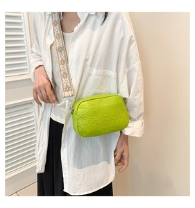 Détail du sac bandoulière vert avec gaufrage rose et large bandoulière tissée