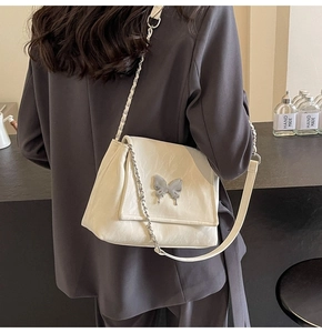 Détail d'un sac bandoulière en cuir plissé blanc crème avec un grand papillon en métal argenté