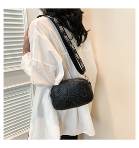 Detail of black PU crossbody bag featuring embossed rose patterns and a wide woven strap