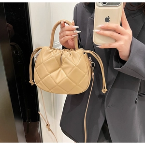 Close-up of beige quilted crossbody bag with drawstring closure and chain strap