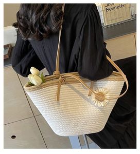 Detail of woven straw tote bag with leather handles and 3D daisy flower decoration