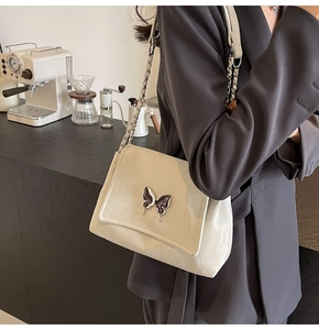 Sac à main crème en cuir PU avec boucle papillon violette porté par un mannequin au café