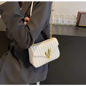 Detailed view of white quilted PU leather bag with gold heart clasp and chain strap