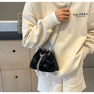 Detail of black pleated bucket bag featuring a silver chain strap and pearl drawstring charms