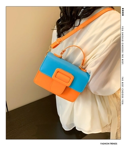 Detail view of contrast color crossbody bag with orange resin buckle and adjustable strap