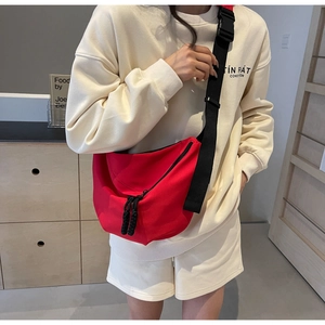 Close-up of a red nylon crescent crossbody bag with double zippers and wide black strap