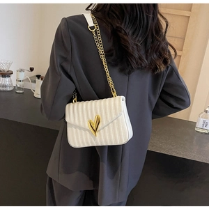 Detailed view of white quilted PU leather bag with gold heart lock and chain strap on model