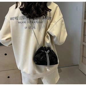 Detail of black drawstring bucket bag featuring silver chain strap and pearl charms