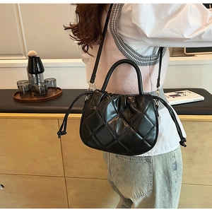 Detail of black quilted PU leather crossbody bag with drawstring design and round handle