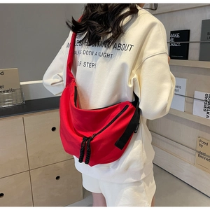 Detail of red canvas crescent bag with black wide strap worn by model in lifestyle setting