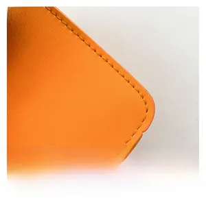 Macro shot of orange pebble leather texture with precise stitching on a small square bag
