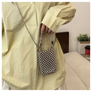 Détail d'un mini sac à perles argentées avec chaîne et poignée métallique sur un modèle