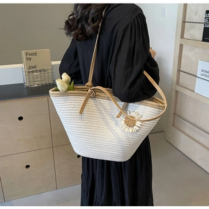 Detail of woven straw tote bag featuring a white daisy flower and knotted leather strap
