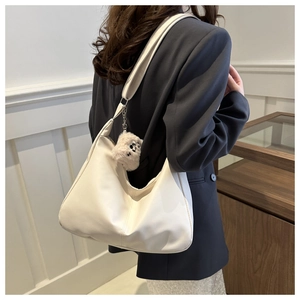 Close-up of minimalist cream PU leather shoulder bag with cute plush puppy charm