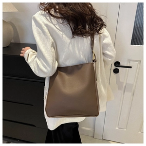 Detail of a large brown PU leather tote bag with metal buckle shown on a model