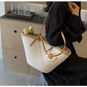 Detail of woven tote bag with white daisy flower and brown leather straps in use