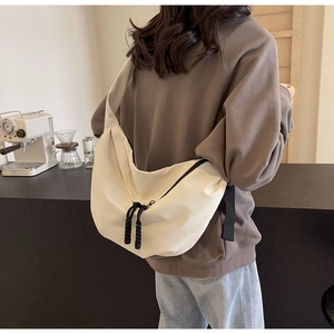 Detail of a creamy white half-moon nylon crossbody bag worn by a model in a modern cafe