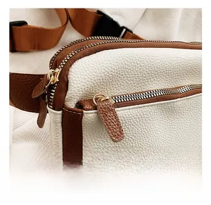 Detail showing high-quality gold zippers and textured pebble leather on a two-tone crossbody bag
