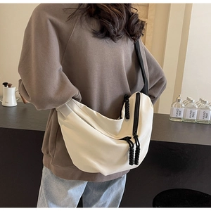 Detail of a beige crescent crossbody bag featuring a black zipper and casual nylon texture