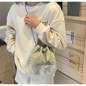 Detail of pistachio green pleated bucket bag with pearl drawstring and metal chain strap