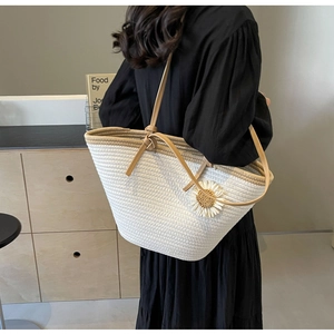 Detail of a white woven straw tote bag with brown straps and a daisy flower decoration