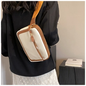 Detail of crossbody bag with beige lychee texture and brown trim showing dual zippers