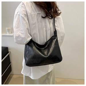 Close-up of black glossy PU leather hobo bag with wide shoulder strap and pleated texture