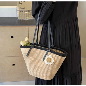 Close-up of woven straw handbag featuring a large white daisy flower and contrast black straps